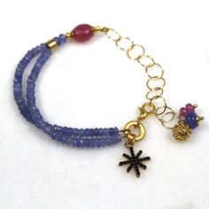 Glittering, vibrantly hued genuine polished natural periwinkle hued tanzanite, one of the rarest and most prized of all gemstones, sparkles on this strand in a beautiful bright striking splash of color! A plump faceted pink sapphire accents the side of the wrist. 14k gold fill chain and colorful drop embellishments add a little chic bling. l Blue Faceted Amethyst Jewelry, Faceted Blue Amethyst Jewelry, Blue Tanzanite Bracelet Jewelry, Blue Tanzanite Gemstone Bracelets, Blue Amethyst Beaded Bracelets As Gift, Blue Amethyst Beaded Bracelets For Gift, Handmade Blue Amethyst Bracelets, Blue Amethyst Bracelets With Natural Stones, Tanzanite Gemstone Bracelet Jewelry