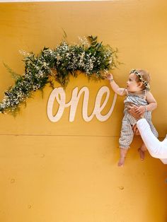 a woman holding a baby in front of a sign with the word one painted on it