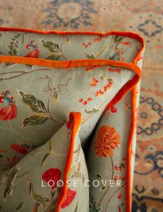 two pillows with orange piping on them in front of a floral carpet and rug