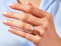 a woman's hand with a diamond ring on her left hand, wearing a blue shirt