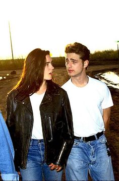 two young people standing next to each other in front of a dirt field at sunset