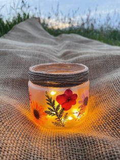 a glass jar with flowers on it sitting on top of a burlied cloth