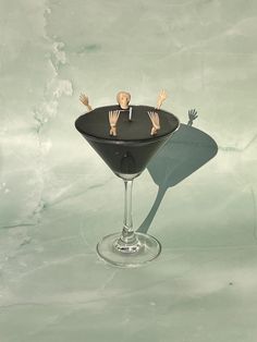 a miniature man sitting in a martini glass with his hands out to the side,