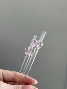 a person holding two clear glass sticks with pink flowers on them