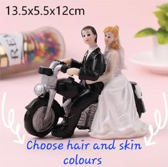 a wedding cake topper with a bride and groom on a motorcycle next to confetti tins