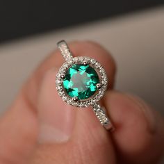 a close up of a person's hand holding a ring with a green stone