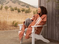 a woman sitting in a white chair with an orange striped blanket on her shoulders and legs