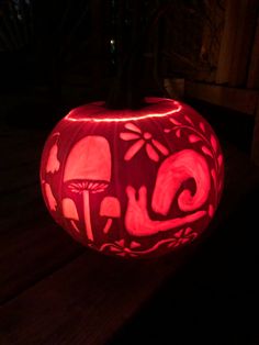 a carved pumpkin sitting on top of a wooden table in the dark, with mushrooms and leaves painted on it