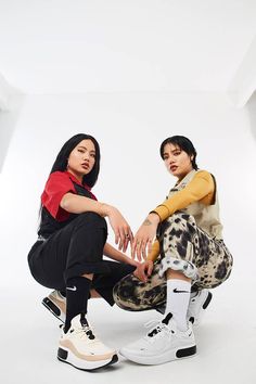 two young women sitting next to each other in front of a white background wearing sneakers