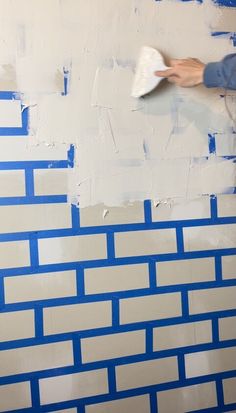 a person painting a brick wall with blue tape and white paint on the walls behind them