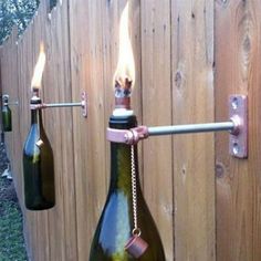 two wine bottles are attached to the side of a wooden fence with lights on them