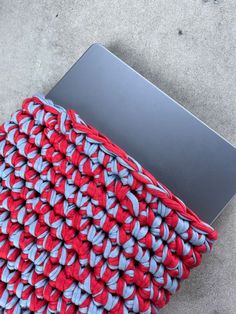 an open laptop computer sitting on top of a red and blue blanket covered in crochet