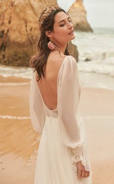 a woman standing on top of a beach next to the ocean wearing a white dress