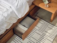 a bed with white sheets and pillows next to a night stand on a carpeted floor