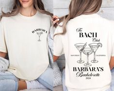 a woman wearing a white t - shirt that says the bachelor club and two martini glasses