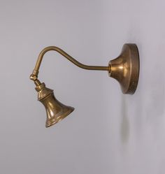 an antique brass wall light on the side of a white wall with a bell attached to it