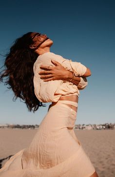 a woman is standing on the beach with her arms around her neck and looking up into the sky