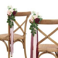 two wooden chairs decorated with flowers and greenery on the back one has a pink ribbon