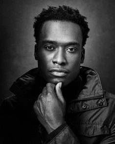 a black and white photo of a man with his hand on his chin looking at the camera