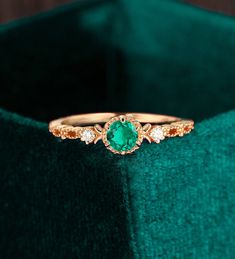 an emerald colored ring sits on top of a green velvet box, with three diamonds around it