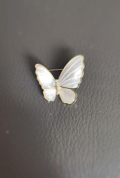 Delicately crafted, this Mother of Pearl Butterfly Brooch is designed with an asymmetrical style, adding a touch of elegance and charm to any outfit. Its petite size makes it suitable for daily wear, adding a subtle yet refined sparkle to your attire. Made with genuine mother of pearl, cubic zirconia, and copper plated in gold, this brooch is a beautiful blend of nature-inspired beauty and luxurious detail. Size: 1.1 in * 1.1 in (Handmade, the actual size can vary) Material: Mother of Pearl, Cub Elegant Silver Enamel Pin For Weddings, White Butterfly Brooches For Gifts, Elegant White Enamel Pin For Gift, Wedding Enamel Pin Brooch, Formal White Enamel Pin Brooch, White Anniversary Brooch Jewelry, Formal White Enamel Pin, Elegant Butterfly Shaped Pins, White Brooch Jewelry Gift