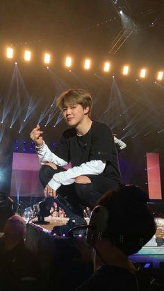 a man sitting on top of a stool in front of a crowd at a concert