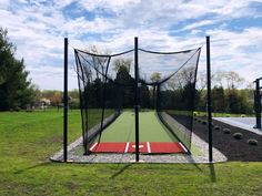 an indoor batting cage in the middle of a field with grass and rocks around it