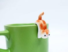 a green coffee mug with a cat sticking out of it's side on a white surface