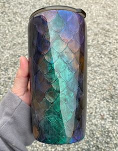 a person holding up a blue and green colored cup with fish scales painted on it