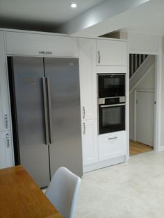 a kitchen with white cabinets and stainless steel refrigerators in the center, along with an open staircase leading up to the second floor