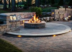 an outdoor fire pit surrounded by stone walls and seating area with lights on each side