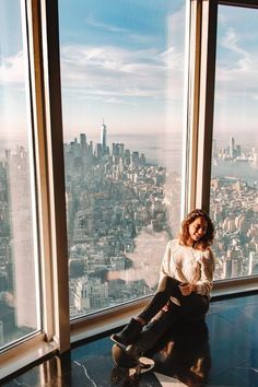 a woman sitting on top of a tall building looking out the window at the city