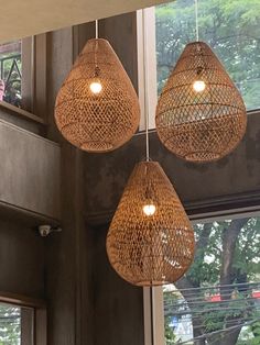 three light fixtures hanging from the ceiling in a room with large windows and trees outside