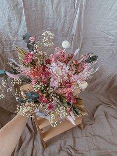 a bouquet of flowers sitting on top of a wooden stand next to a person's hand