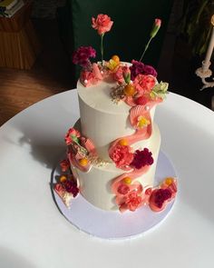 a three tiered white cake with flowers on the top and bottom, sitting on a table