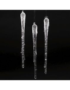 three ice - like objects hanging from strings in the dark, with snow on them