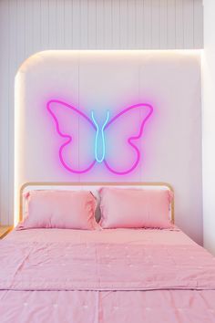 a pink bed with a butterfly neon sign above it