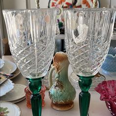 two green glass vases sitting on top of a table next to plates and bowls