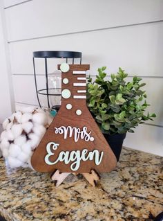 a wooden sign sitting on top of a counter next to cotton balls and a potted plant