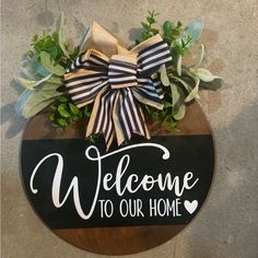 welcome to our home sign with greenery and bow hanging on the front door hanger