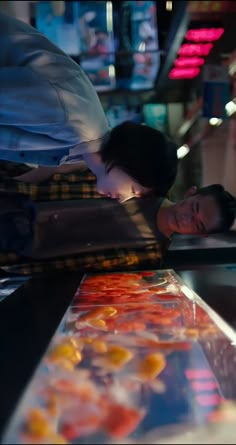 two people standing next to each other in front of a display case with oranges on it