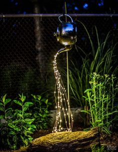 a metal watering can with fairy lights on it in the middle of a garden at night