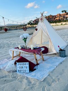 a teepee sitting on top of a sandy beach next to a vase filled with flowers