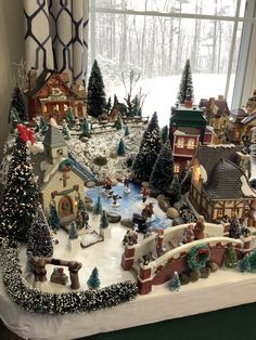 a christmas village is displayed in front of a window with snow on the ground and trees