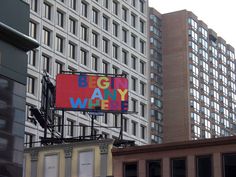 a big sign on the side of a building in front of tall buildings with windows