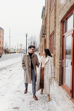 a man and woman are walking down the street in front of a brick building on a snowy day