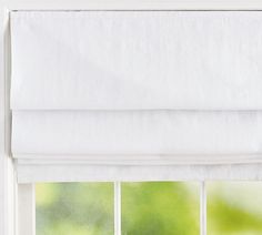 a window with white roman blinds in front of it and green trees outside the window