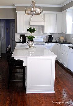 a kitchen with white cabinets and an island in the middle of the room, along with two black bar stools