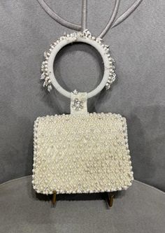 The Joel design pays homage to heritage jaali work, capturing its mysterious play of light and shadow through intricate pearl and beadwork. Natural pearl drops enhance its graceful demeanor. Our mini trapezium bag is a compact and edgy silhouette. This flap over is designed with soft edges. The embellished attached round handle makes it a statement hand held bag. This collectible accessory fits in your valuables like makeup, keys, currency and cards. Elegant White Rectangular Jewelry, Traditional White Jewelry For Evening, Elegant Embellished Jewelry For Events, Traditional White Evening Jewelry, Rectangular White Jewelry With Pearl Drop, Luxury White Beaded Jewelry, Evening Pearl Jewelry Embellished, Luxury Beige Jewelry For Formal Occasions, Evening Embellished Pearl Jewelry