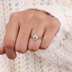 a woman's hand wearing a gold ring with a white diamond in the middle